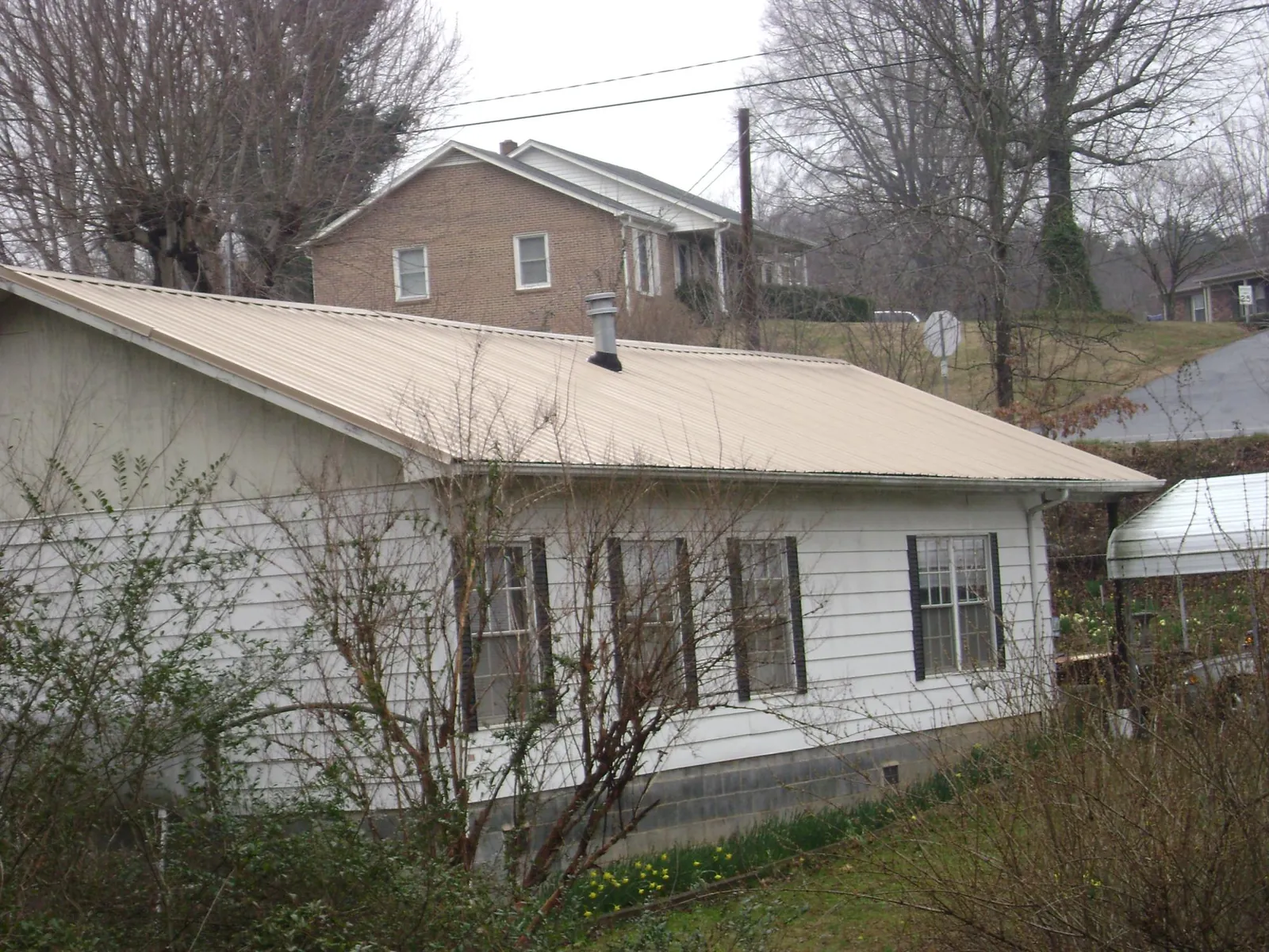 Tan metal roof on a white sided house set into a hillside — Commercial Roofing by Roofing Brothers in Sparkill
